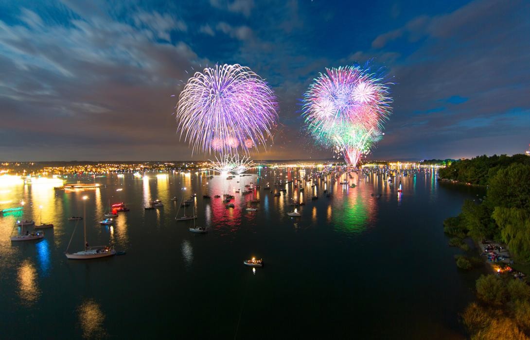 Feuerwerk über dem See, man sieht viele beleuchtete Boote auf dem Wasser