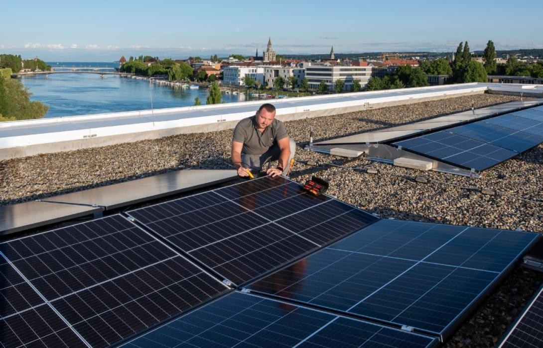 Mann auf einem Dach, während er Photovoltaik-Module installiert