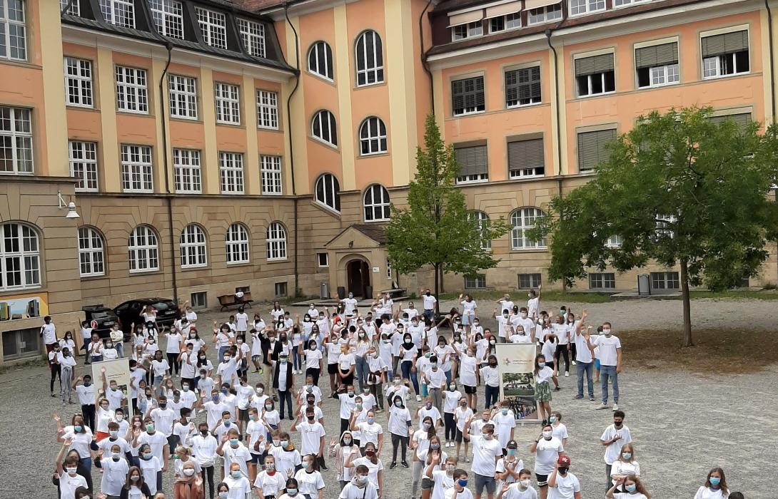 Viele Menschen in weißen Shirts stehen vor einen Gebäude, dem Suso-Gymnasium
