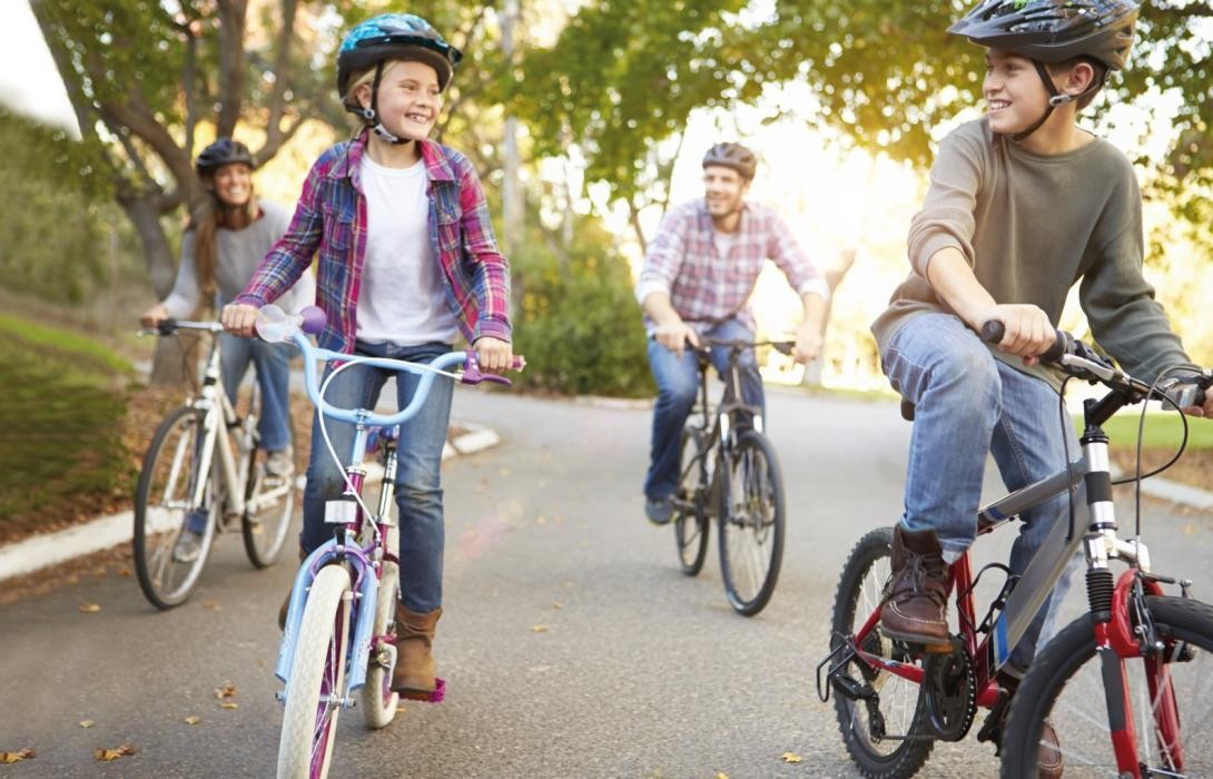 Familie mit zwei Erwachsenen und zwei Kindern fährt auf Fahrrädern eine Straße entlang
