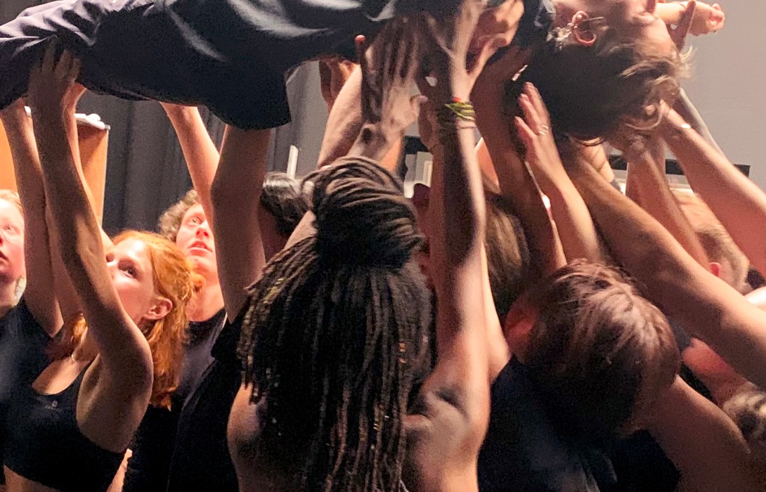 Eine Gruppe Menschen stehen zusammen, tragen auf den nach oben gestreckten Armen eine Person auf dem Rücken.
