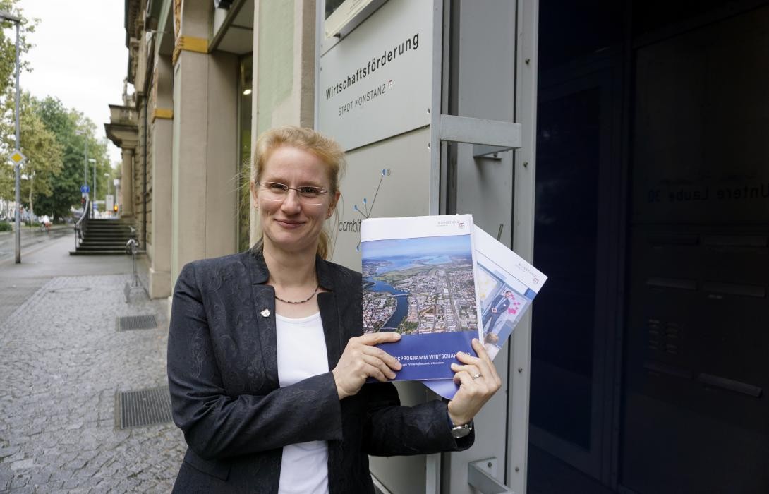 Christina Groll mit einigen Broschüren. Sie steht vor dem Verwaltungsgebäude Laube, in dem die Wirtschaftsförderung angesiedelt ist