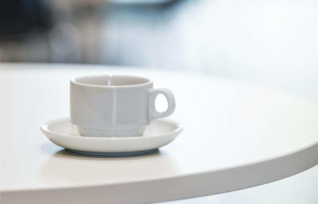 Weiße Kaffeetasse auf einem weißen Tisch vor verschwommenen Hintergrund