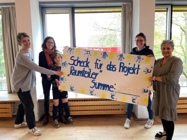 Vier Frauen halten einen Scheck auf dem "Scheck für das Projekt Raumteiler, Summer 2333,33 €" steht