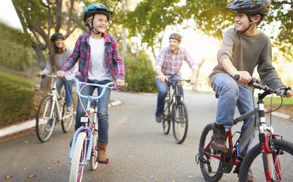 Familie mit zwei Erwachsenen und zwei Kindern fährt auf Fahrrädern eine Straße entlang