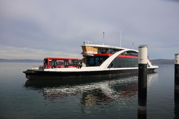 Ein Fährschiff auf dem Wasser. Vorne auf dem Schiff parkt ein roter Bus.