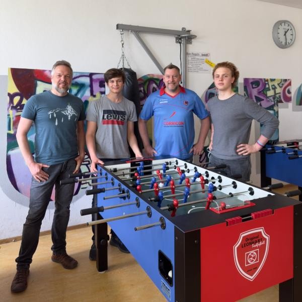 Vier Männer stehen hinter einen blau roten Kicker Tisch
