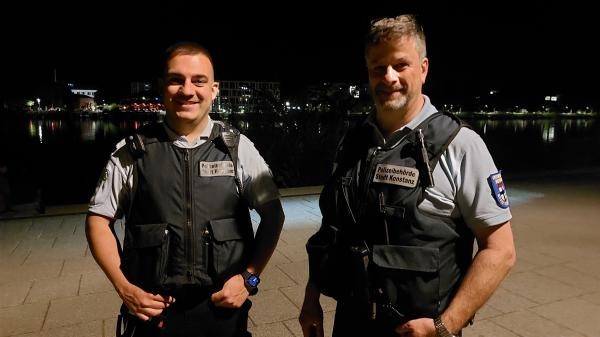 Zwei Männer stehen nachts am Seerhein, tragen Schutzwesten und das Abzeichen der Kommunalen Ordnungsdienstes.
