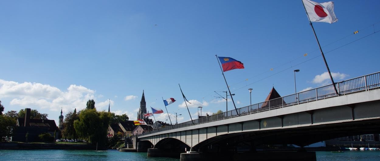 Internationale Flaggen wehen an einer Brücke, die über einen Fluss führt