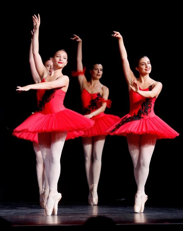 Drei Ballerinas in roten Kleidern vor schwarzem Hintergrund.