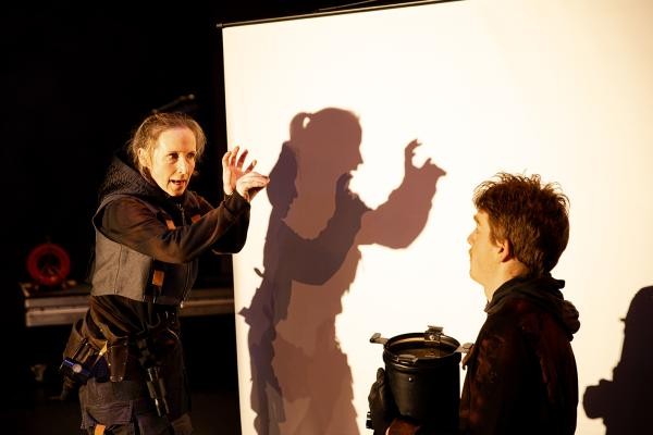 Zwei Personen vor einer Leinwand schauen sich, eine formt Schattenfiguren mit ihren Händen.
