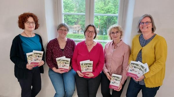 Fünf Frauen stehen im Innenraum an einem Fenster und halten je eine der Broschüren in den Händen