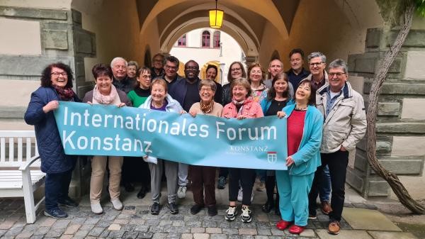 Gruppe Personen steht in einem Torbogen. Sie halten ein hellblaues Banner mit Schriftzug Internationales Forum Konstanz
