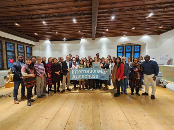 Gruppe Menschen im Innenraum hält ein Banner. Darauf zu lesen: Internationaler Ausschuss Stadt Konstanz
