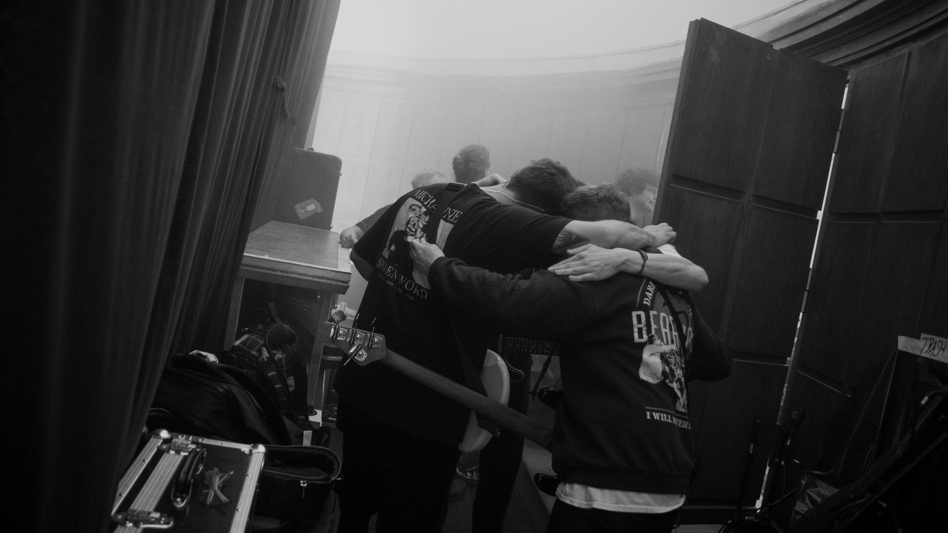 Ein Gruppe Musiker hinter der Bühne halten sich im Arm und schwören sich vor dem Auftritt ein