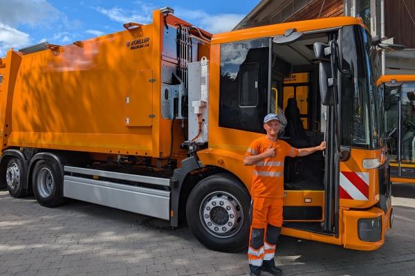 Mann in orangener Arbeitsbekleidung vor einem orangenen Müllabfuhrfahrzeug