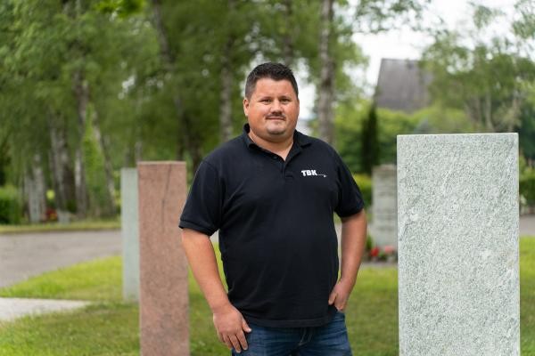 Ein Mann mit Bart ist neben zwei unbeschrifteten Grabstelen zu sehen.