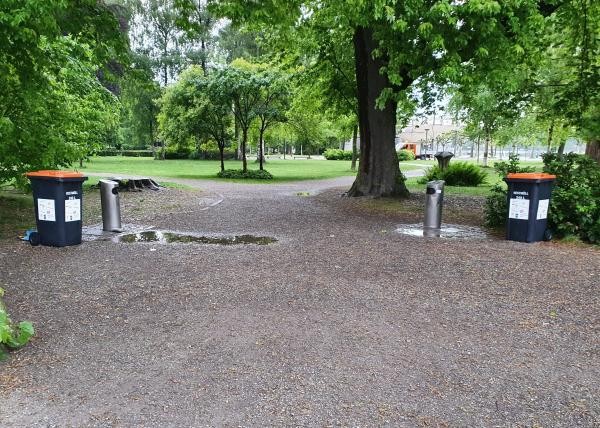 Blick in einen Park mit öffentlichen Mülleimern am Rand des Wegs