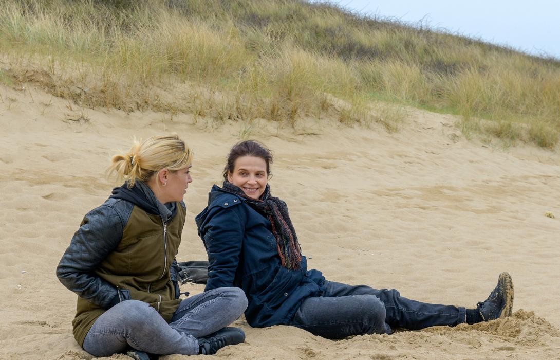 Zwei Frauen sitzen im Sand an einer Düne.
