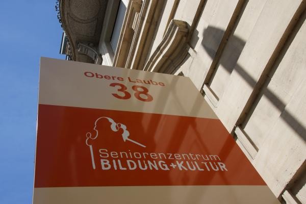 Auf dem Bild ist zu sehen ein Schild, das an der Fassade eines Gebäudes angebracht is. Darauf zu sehen sind die Informationen zum Seniorenzentrum.