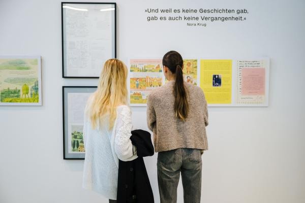 Zwei Personen stehen vor einer Wand mit ausgestellten Illustrationen.