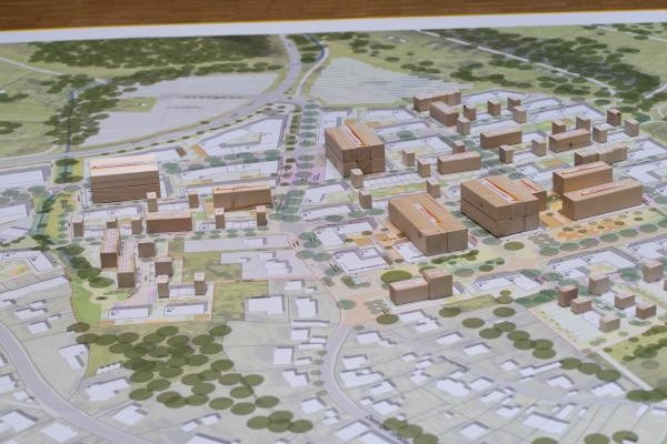 Plan mit architektonischen Zeichnungen von Häusern, Straßenzügen und Bäumen, darauf sind Holzklötze verteilt, die verschiedene Häuserblöcke imitieren.