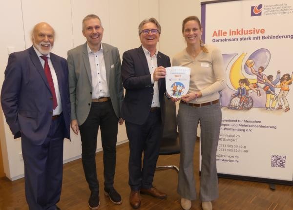 Drtei Männer und eine Frau im Innenraum. Zwei Personen halten eine Plakette.