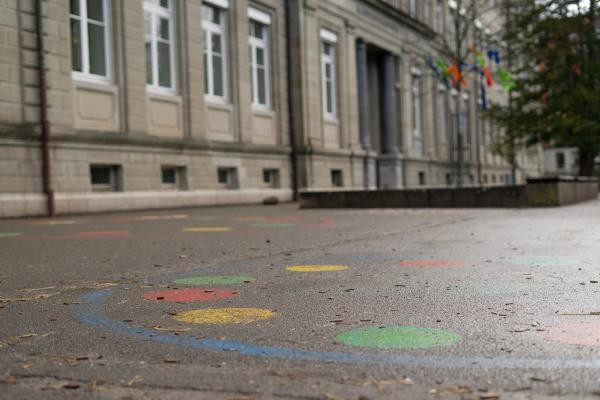 Bild von einem Schulhof, das Schulgebäude im Hintergrund, bunte Kreise auf dem Boden