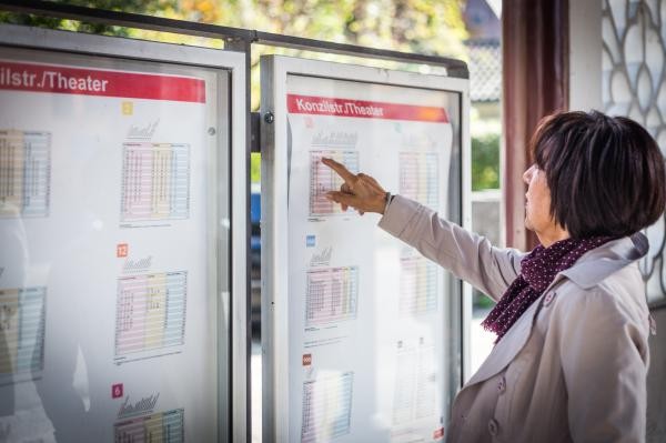 Eine Frau deutet mit einem Finger auf Fahrpläne an einer Haltestelle