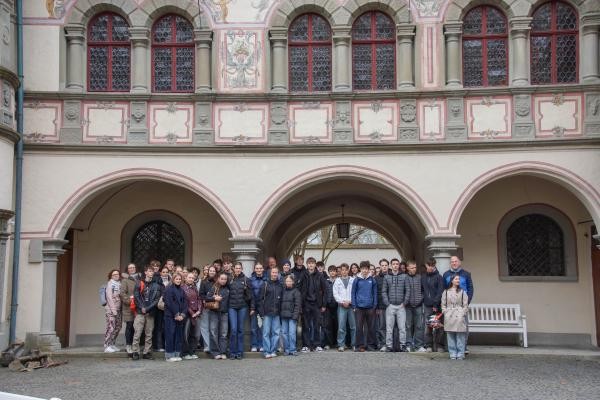 Viele Menschen stehen vor einem historischen Gebäude mit Torbögen und Fenstern