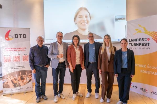 Copyright Stadt Konstanz Gruppenfoto der Verantwortlichen der Pressekonferenz zum Landesturnfest 2026 in Konstanz. Im Hintergrund sind die Roll-ups des Badischen Turner-Bunds und des Landesturnfests sowie eine per Video zugeschaltete Person auf einer Leinwand zu sehen.