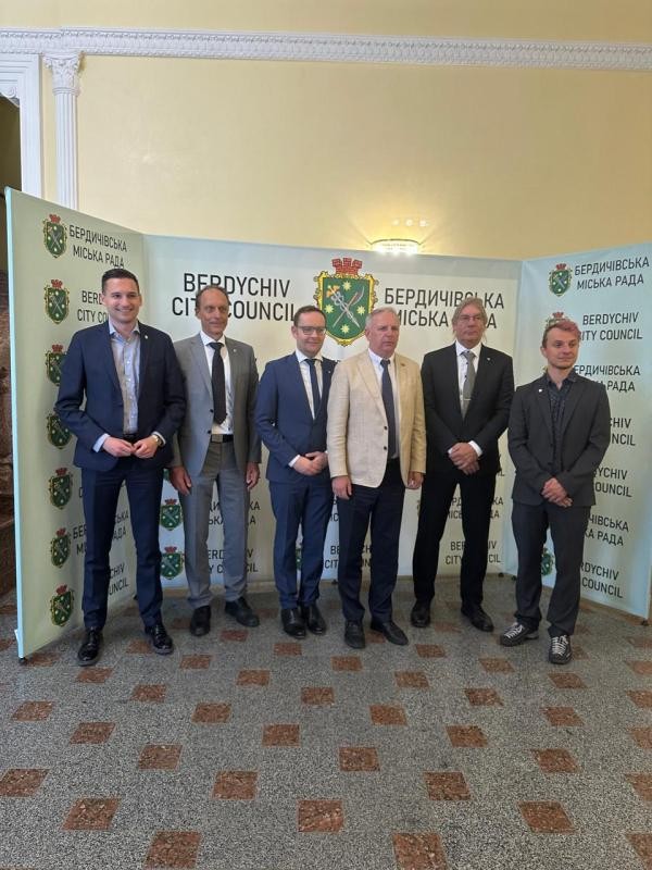 Die Konstanzer Delegation steht bei einem Besuch beim Berdytschiwer Stadtrat für ein Gruppenfoto vor einer Wand mit dem Wappen und Schriftzug „Berdychiv City Council". Sechs Männer in Anzügen posieren nebeneinander in einem historischen Saal.
