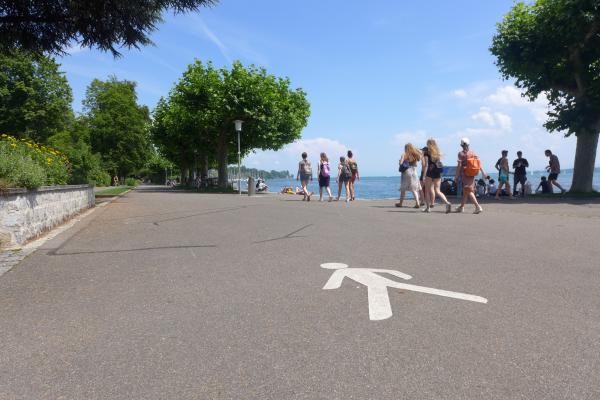Fußgänger-Markierung auf einer Straße; im Hintergrund vorbeilaufende Menschen