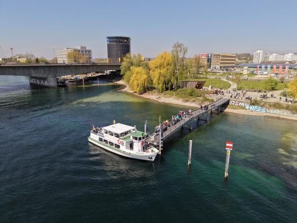 Luftaufnahme: Der Wasserbus „Seeperle" legt an einem langen Steg am Konstanzer Bodanufer an, mehrere Fahrgäste gehen über den Steg. Im Hintergrund sind eine Brücke, das Bodenseeforum sowie der grüne Uferpark mit Spaziergängern zu sehen.