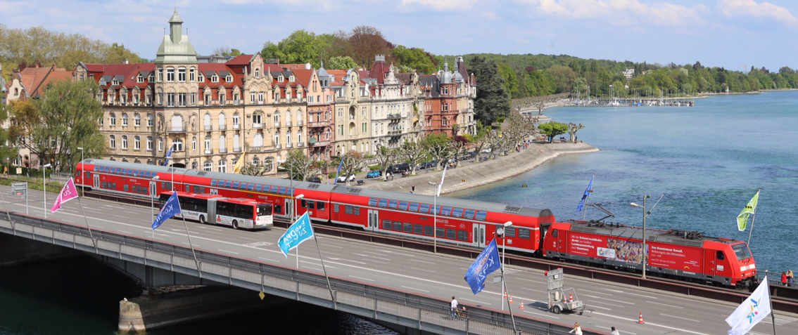 Ein Zug fährt über die alte Rheinbrücke, im Hintergrund die Häuser der Seestraße
