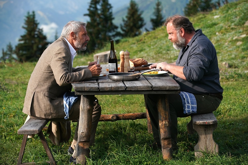 Zwei Männer sitzen an einem Tisch auf einer Wiese und essen.