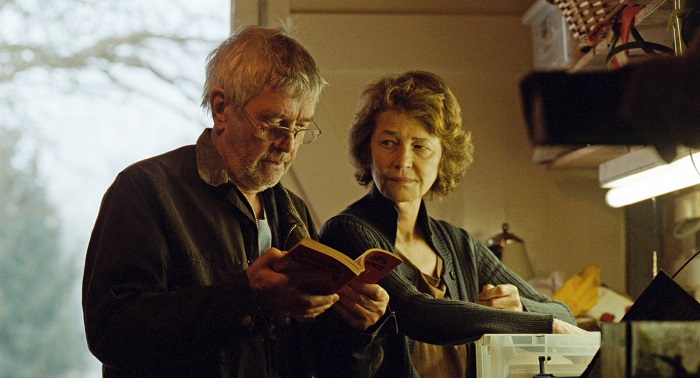Ein älteres Paar steht in der Küche, er hält ein aufgeschlagenes Buch in der Hand, beide blicken hinein.